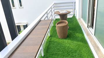 A balcony with artificial grass, a wooden table, and a wicker chair.