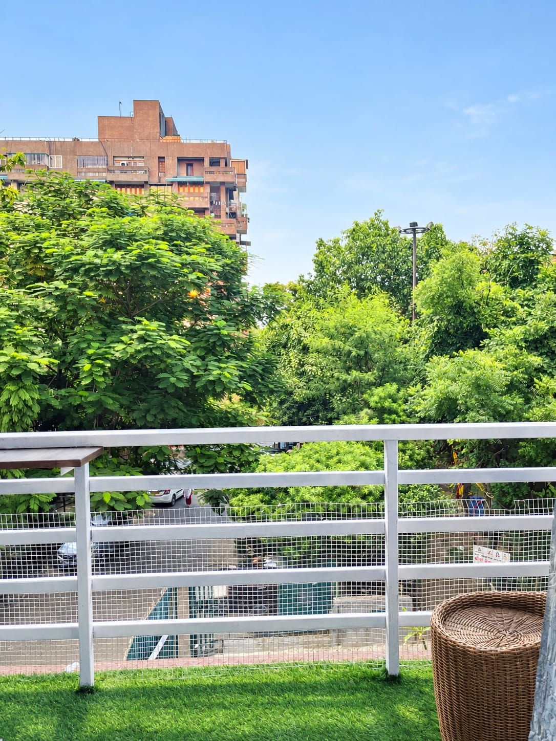 A balcony with a white railing, a wicker basket, and a view of a building and trees.