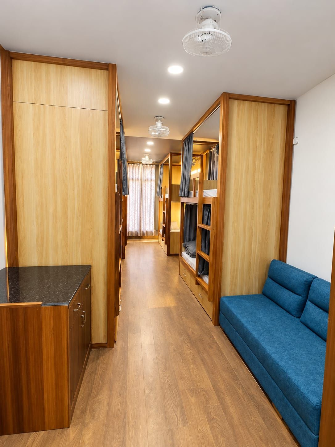 A narrow hallway with wooden walls, a blue sofa, and a kitchenette area.