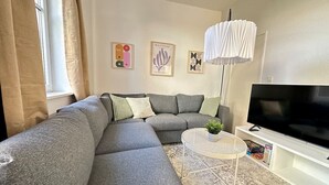 Una sala de estar moderna con un sofá seccional, una mesa de centro redonda, un televisor de pantalla plana y obras de arte en la pared.
