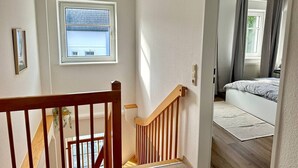 Una escalera conduce a un dormitorio con una cama, un ventanal y una puerta.
