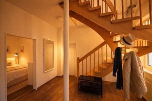 Una habitación con escalera de madera, una cama, una mesa y un perchero con un sombrero.