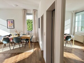 Un salon moderne avec un coin repas, de grandes fenêtres et une vue sur la verdure environnante.