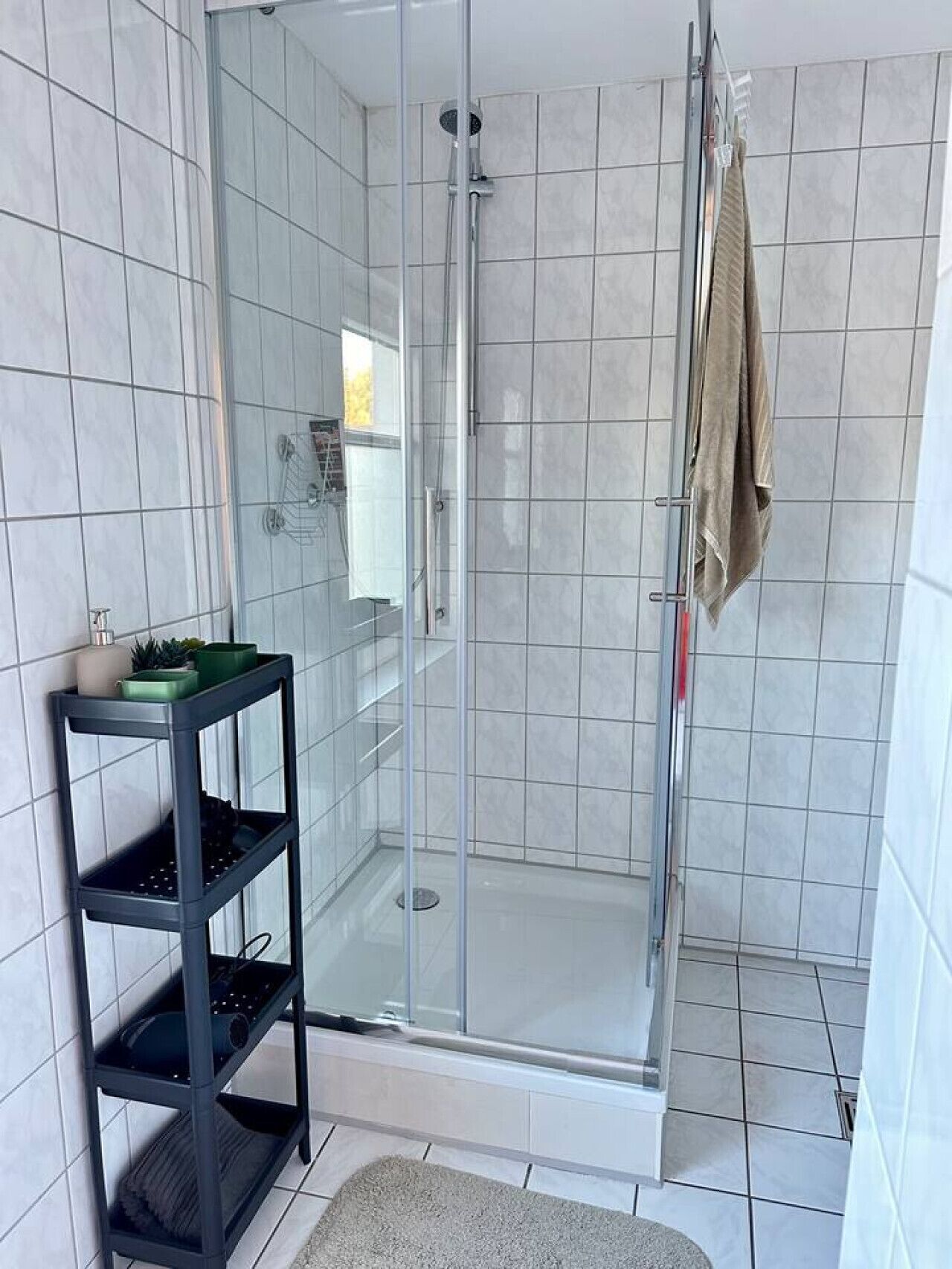 A modern bathroom with a glass-enclosed shower, a black shelf with toiletries, and a beige towel hanging on the wall.