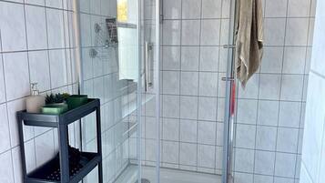 A modern bathroom with a glass-enclosed shower, a black shelf with toiletries, and a beige towel hanging on the wall.