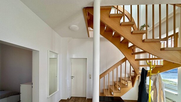 Un interior moderno con una escalera de madera, una cama, un armario blanco y vistas al mar.