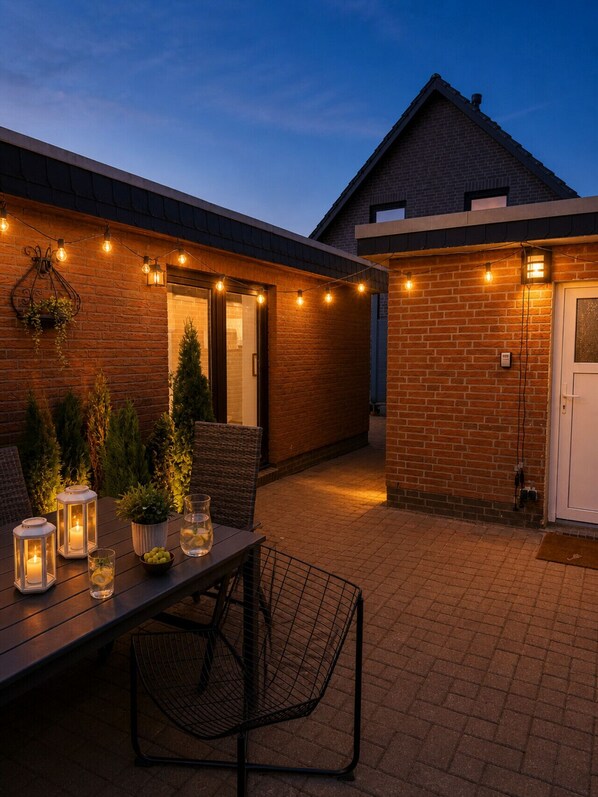 Eine Terrasse mit Tisch, Stühlen, Lichterkette und Blumentöpfen.