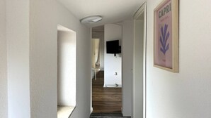 Un couloir avec un luminaire au plafond, un tableau encadré accroché au mur et un escalier menant à une autre pièce.