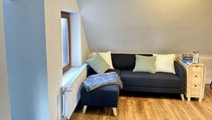 Une pièce chaleureuse avec un canapé sombre, une petite table de chevet en bois et un radiateur.