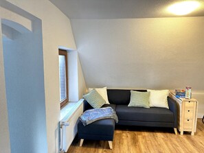 Ein gemütliches Zimmer mit einem dunklen Sofa, einem kleinen Nachttisch und einer Heizung.