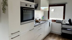 Une cuisine compacte avec des meubles blancs, un four à micro-ondes, une cuisinière et une fenêtre donnant sur un toit recouvert de tuiles.