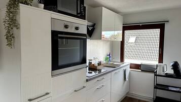 A compact kitchen with white cabinetry, a microwave, a stove, and a window with a view of a tiled roof.