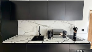 Eine moderne Küche mit Marmorarbeitsplatte, einer Kaffeemaschine, einem Toaster und schwarzen Schränken.