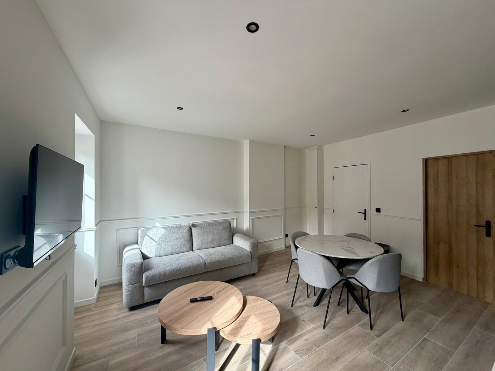 Ein modernes Wohnzimmer mit einer Couch, einem Esstisch mit Stühlen, einem Fernseher und Holzboden.