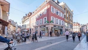 Eine Straße mit Cafés und Apotheken, sowie eine Apotheke auf der anderen Straßenseite.