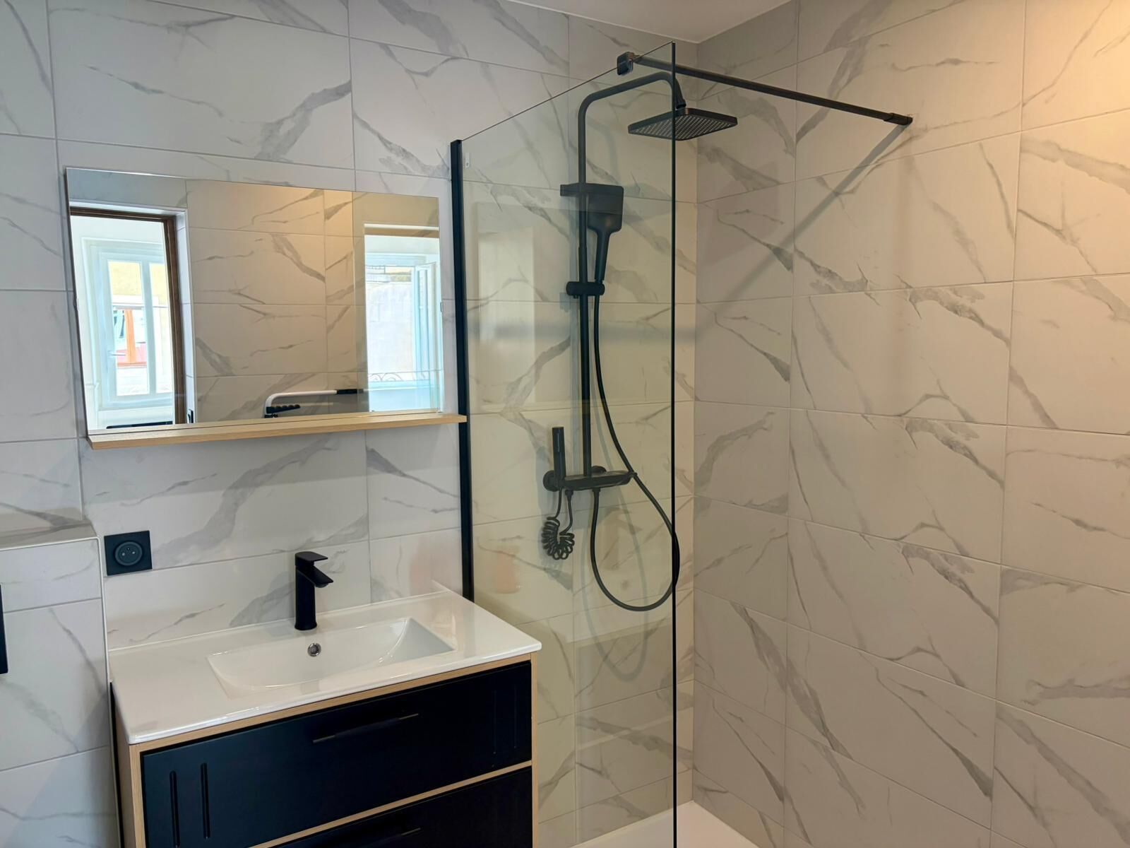 A modern bathroom with a glass-enclosed shower, a white sink, and a mirror above it.