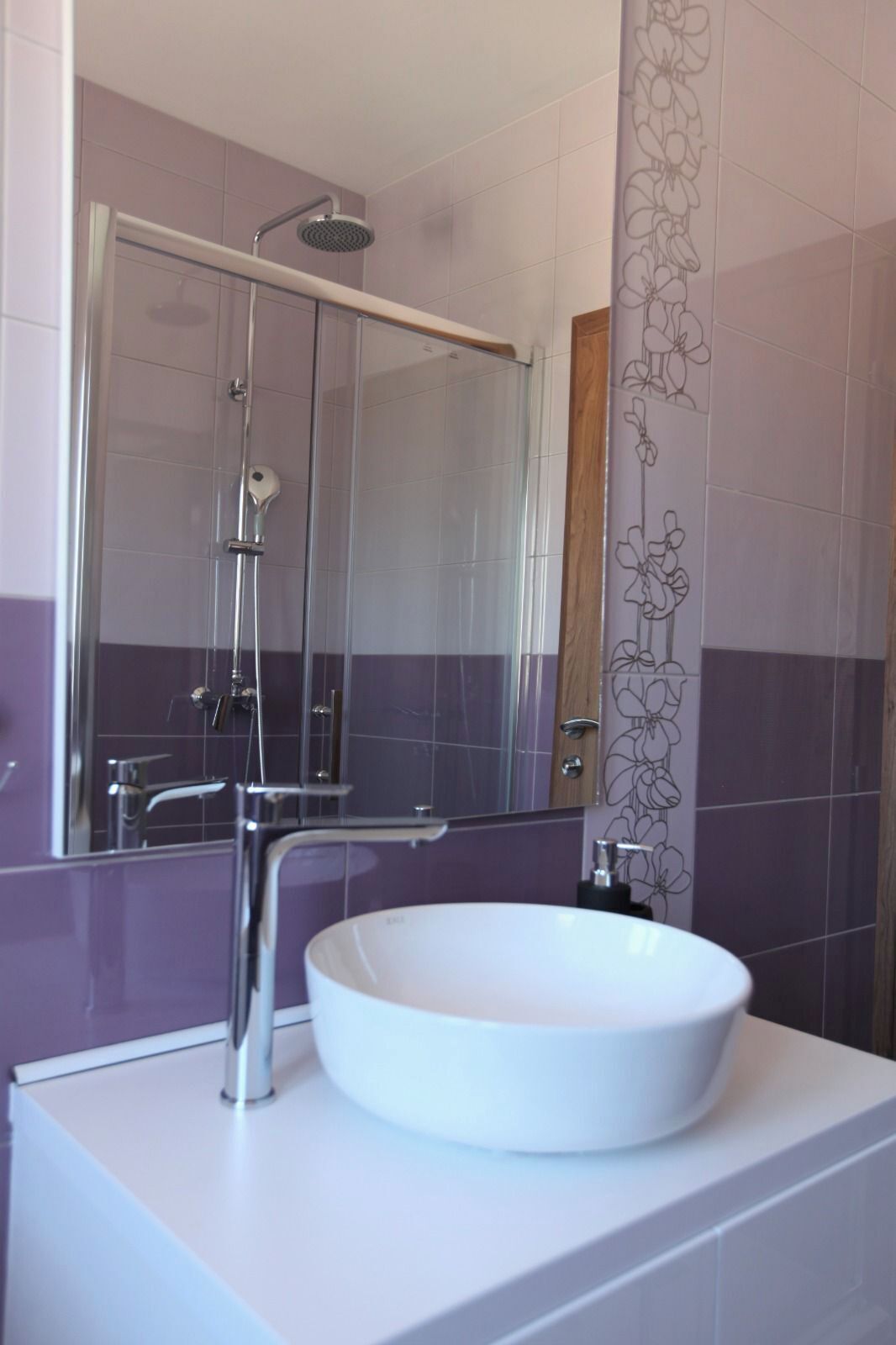 Une salle de bain avec un lavabo blanc, une cabine de douche en verre et des murs recouverts de carreaux violets.