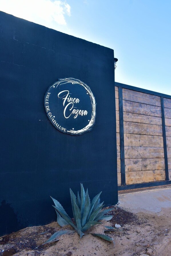 En mørkeblå væg med et rundt skilt, der viser teksten 'Finca Cazosa' og 'Valle de Guadalupe'.