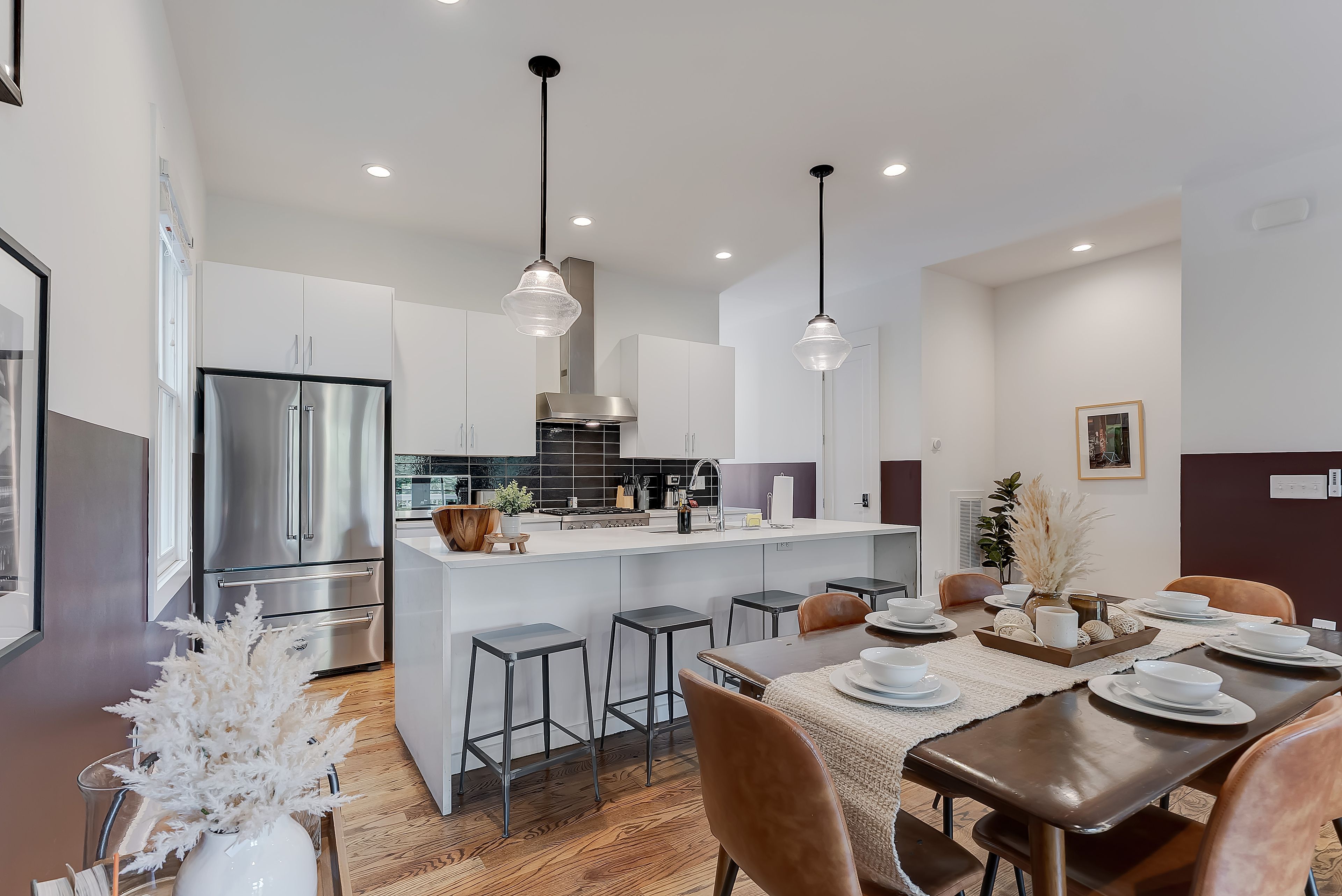 A modern kitchen with stainless steel appliances, a central island, pendant lighting, and a dining area with a table set for four.