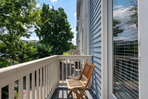 A wooden deck with a single chair, a railing, and a building with vertical siding. - Monroe Houses (Nashville)