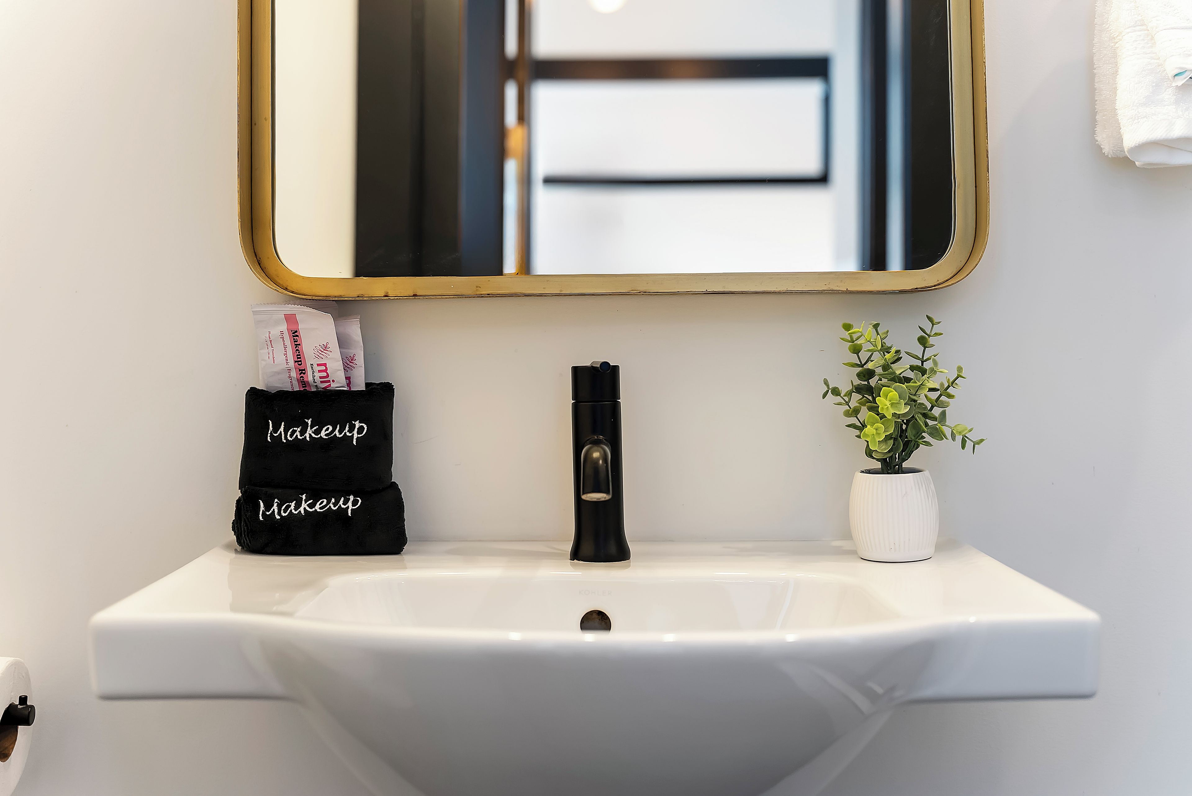 A bathroom sink with a white basin, a black faucet, a small potted plant, and a black towel with 'Makeup' embroidered on it.