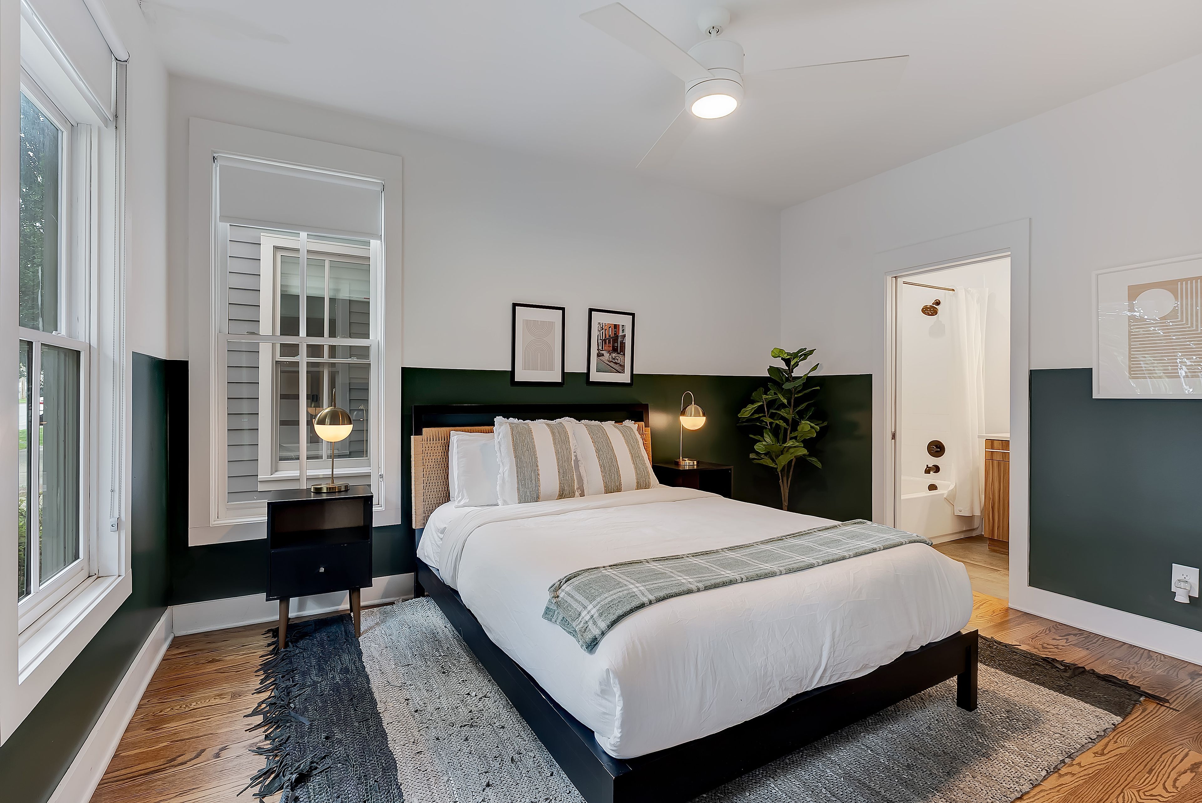 Une chambre à coucher avec un lit, des tables de chevet, un ventilateur de plafond et une grande fenêtre.
