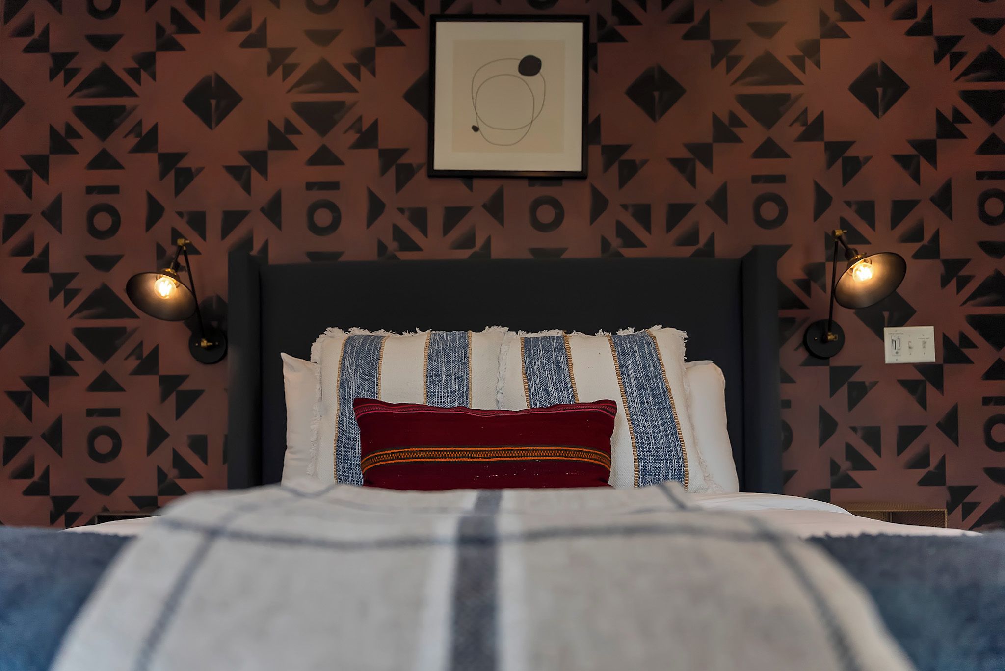 A bed with a headboard, pillows, and a blanket. There are two wall-mounted lamps on either side of the bed.