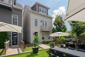 Una casa de dos pisos con un patio, mobiliario exterior y una zona de barbacoa.