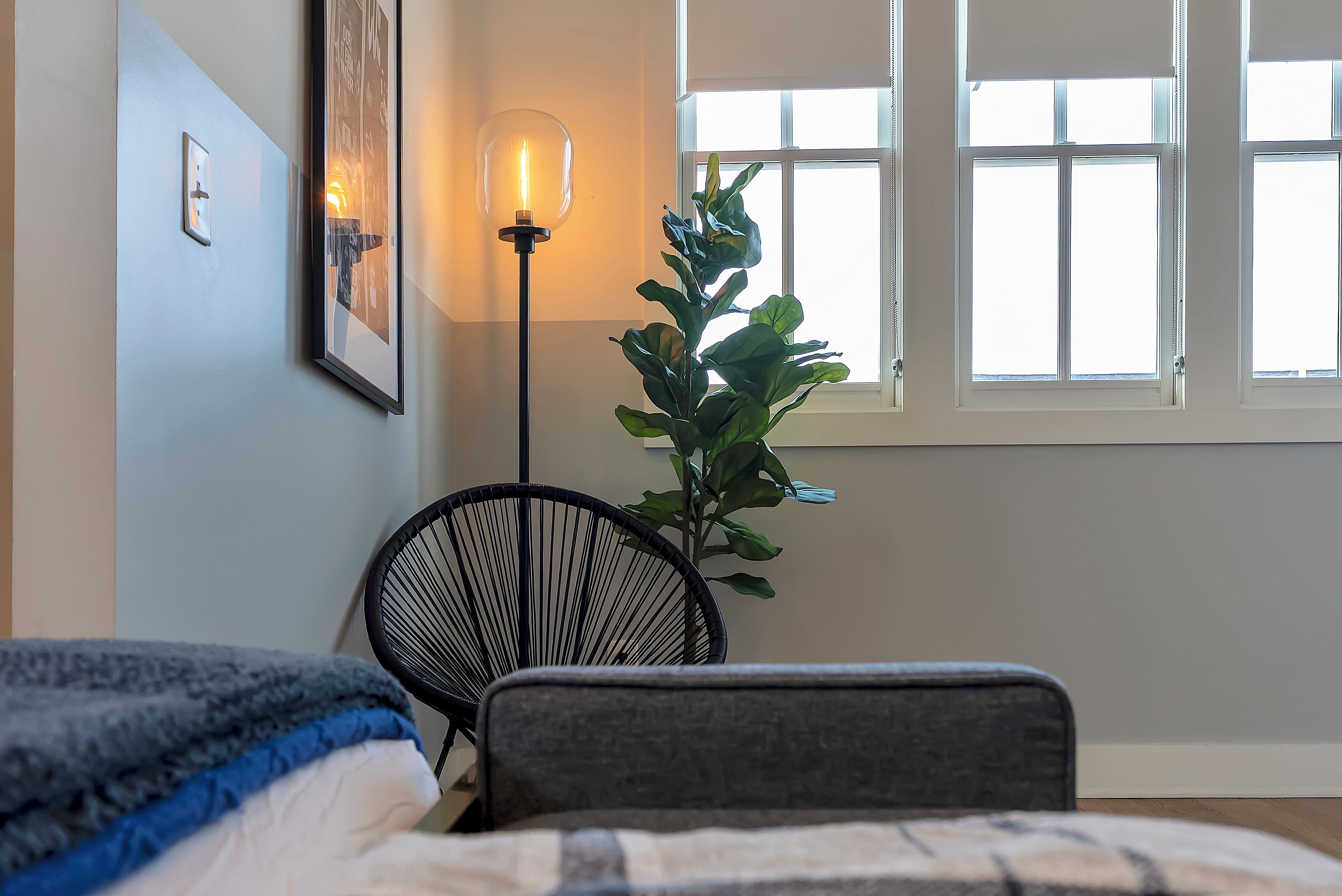 A bedroom with a bed, a chair, a floor lamp, a potted plant, and a window.