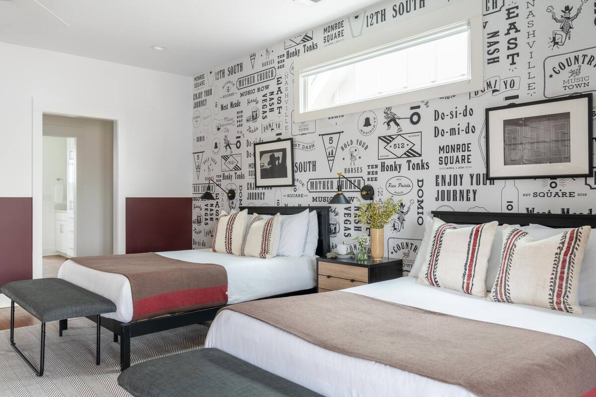 A hotel room with two beds, a large window, and a wall decorated with various city names and symbols.