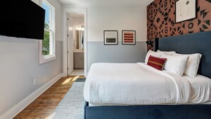 Un dormitorio con cama, cabecera, ventana y puerta que da a un baño.