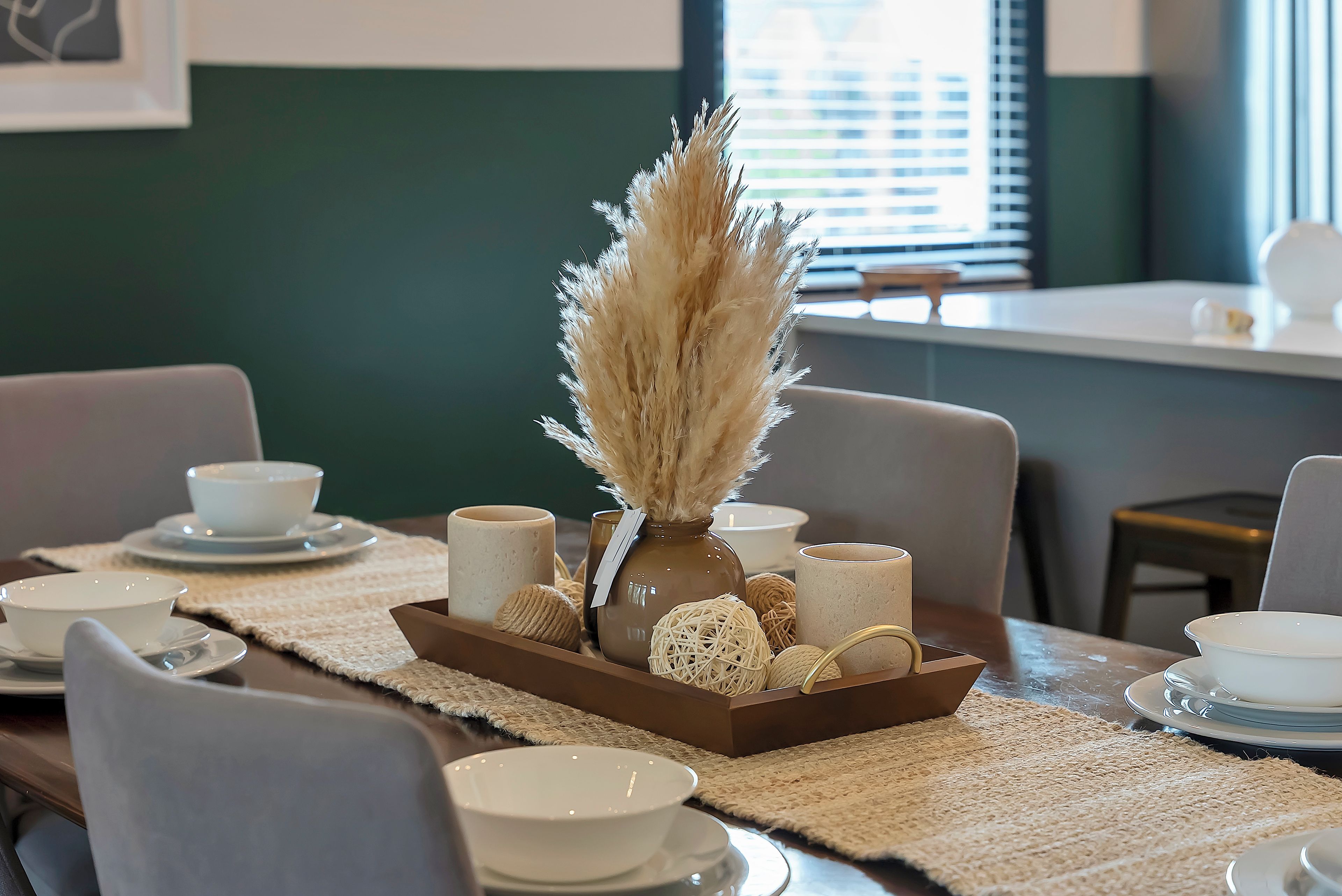 Una mesa de comedor dispuesta con cuencos, platos y un centro de mesa de pastos secos en un florero de cerámica.