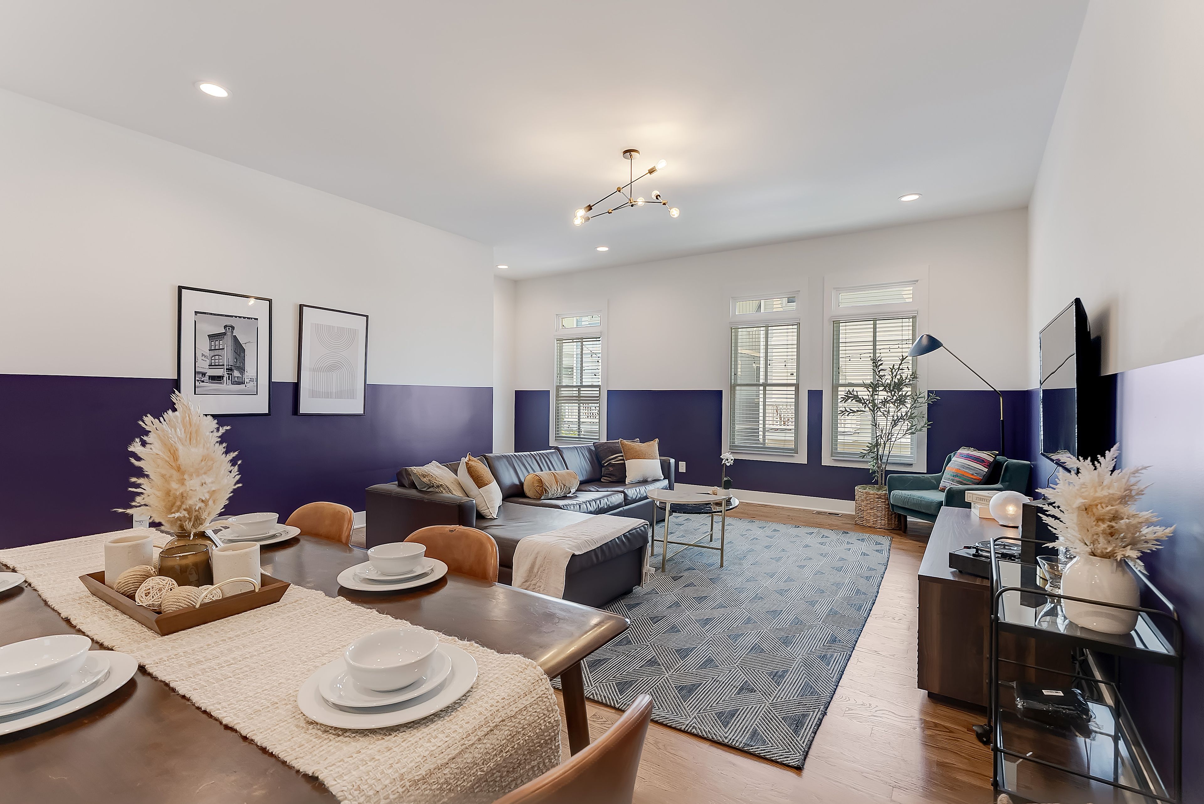 Uma sala de estar moderna com área de jantar, incluindo um sofá, uma mesa de centro e uma mesa de jantar posta com pratos e tigelas.