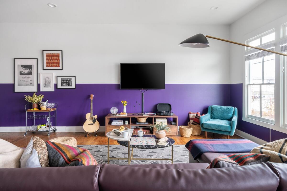 A living room with a purple accent wall, a mounted TV, a blue armchair, and a wooden entertainment unit.