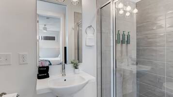 A modern bathroom with a glass shower enclosure, a white sink, and a vanity mirror.