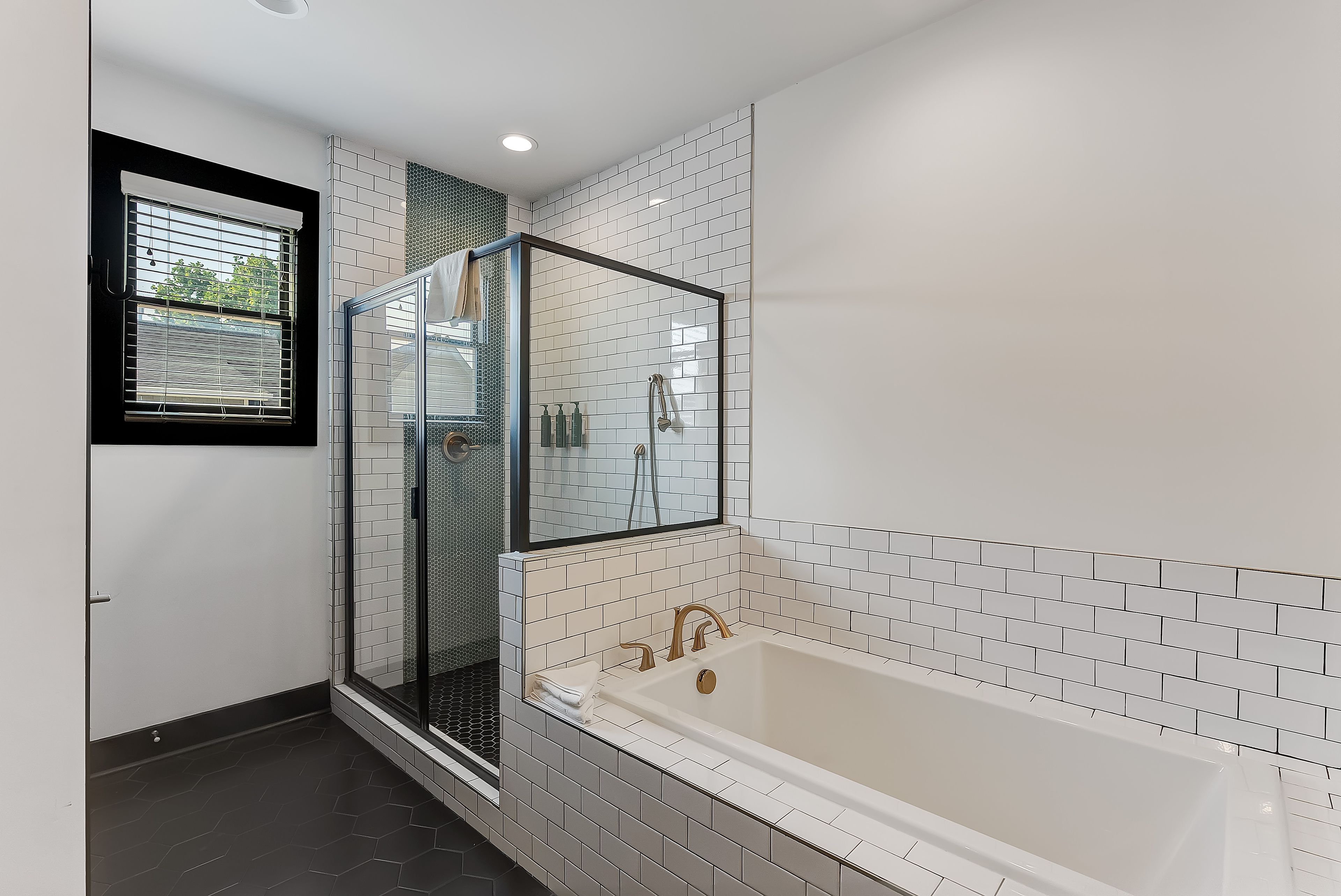 A modern bathroom with a glass-enclosed shower, a large bathtub, and a window with blinds.