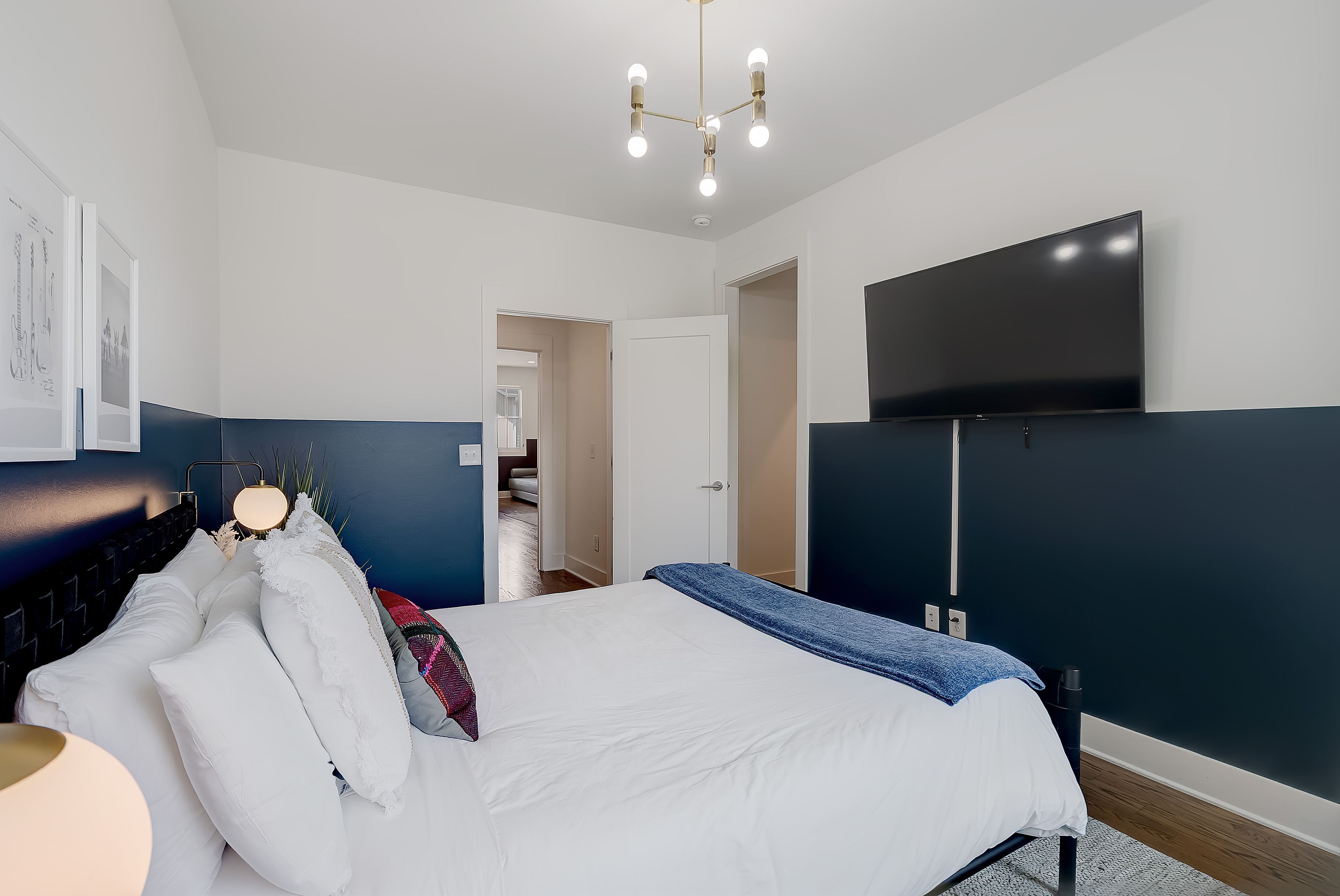 A modern bedroom with a bed, a flat-screen TV mounted on the wall, and a ceiling light fixture.