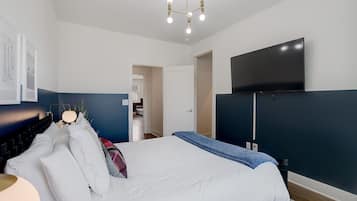 Un dormitorio moderno con cama, televisor de pantalla plana montado en la pared y lámpara en el techo.