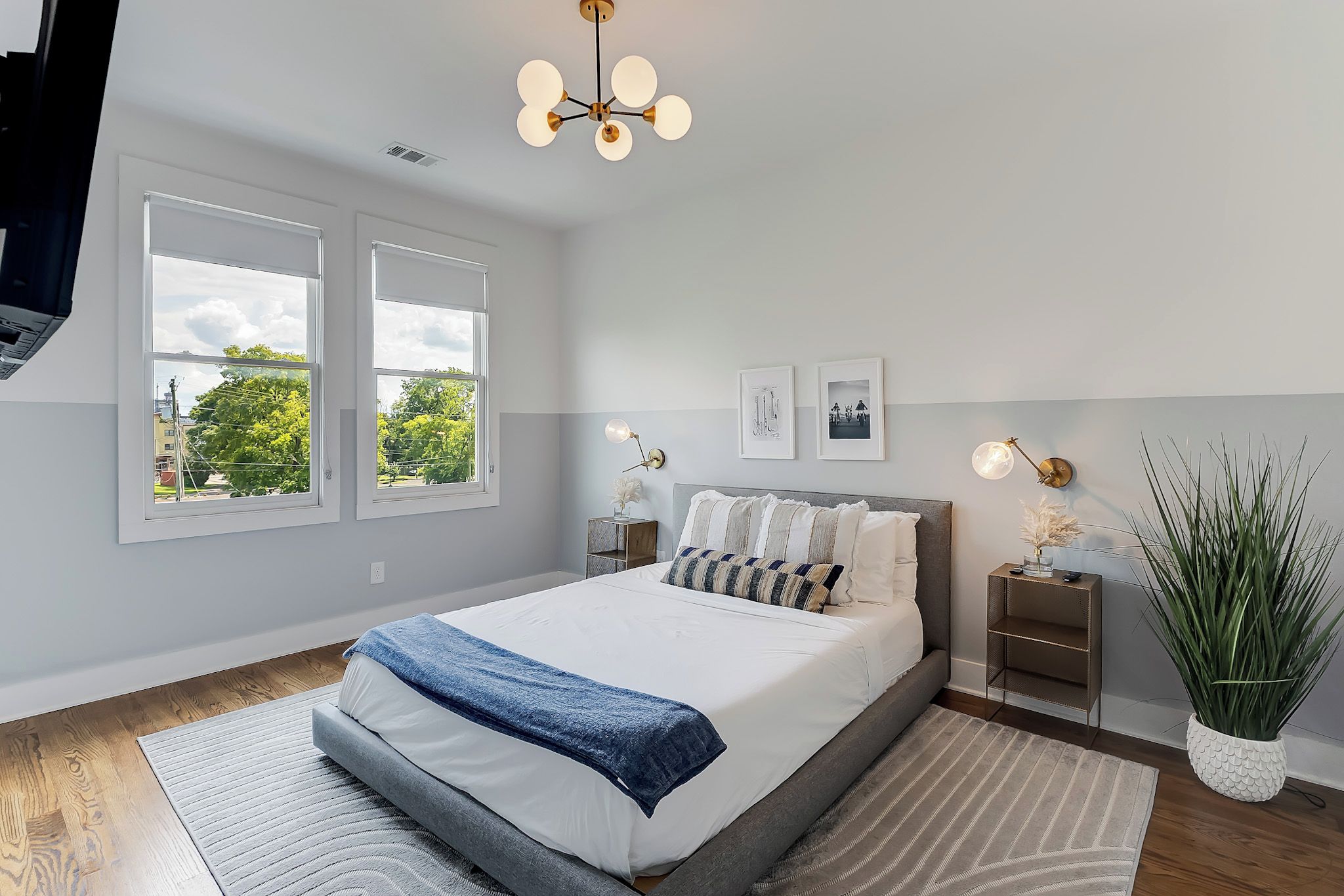 Une chambre à coucher moderne avec un grand lit, deux tables de chevet, un luminaire au plafond et une fenêtre donnant sur des arbres.
