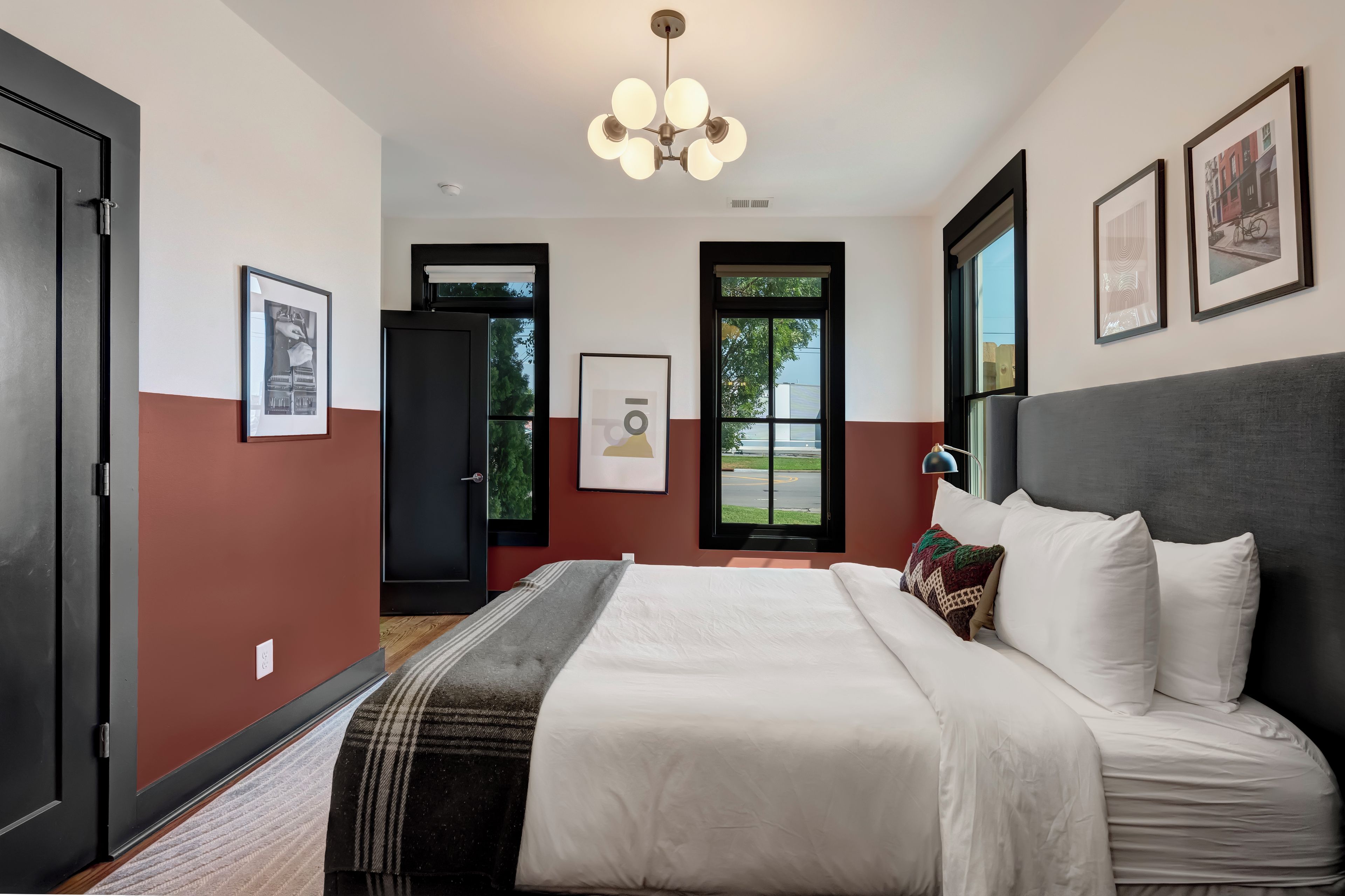 A hotel room with a bed, a window with a view, a door, and a ceiling light fixture.