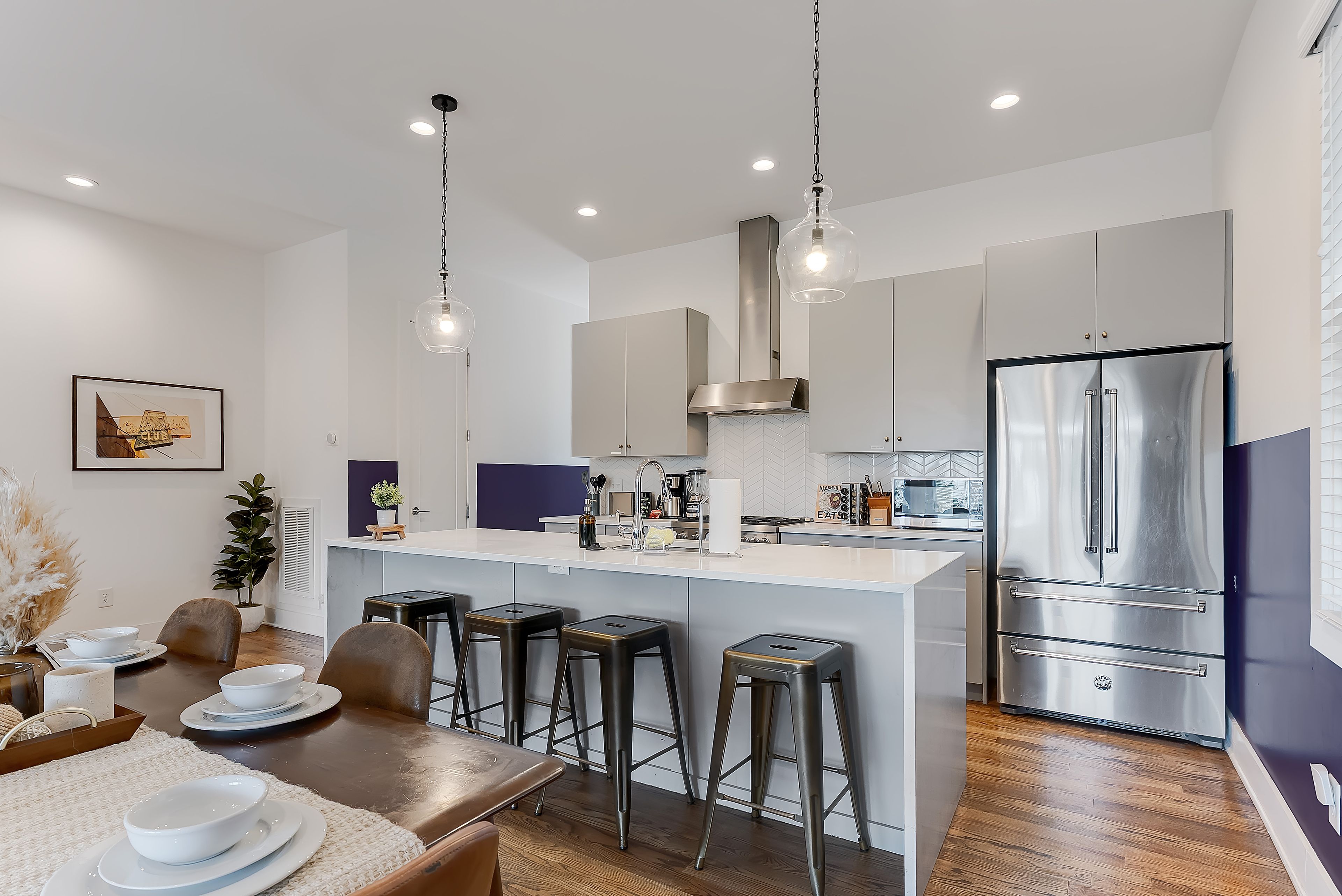 A modern kitchen with a central island, bar stools, stainless steel appliances, and pendant lighting.