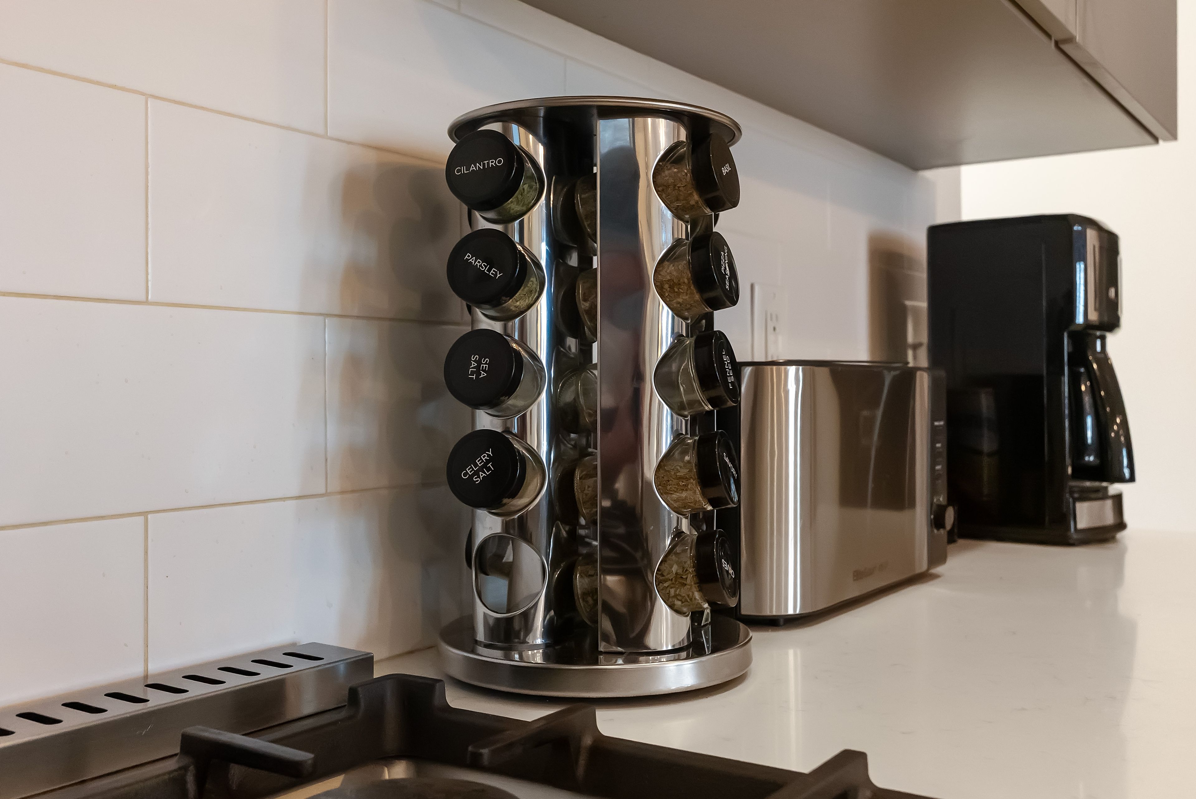 A kitchen with a stainless steel spice rack holding various spices and a coffee maker on the counter.