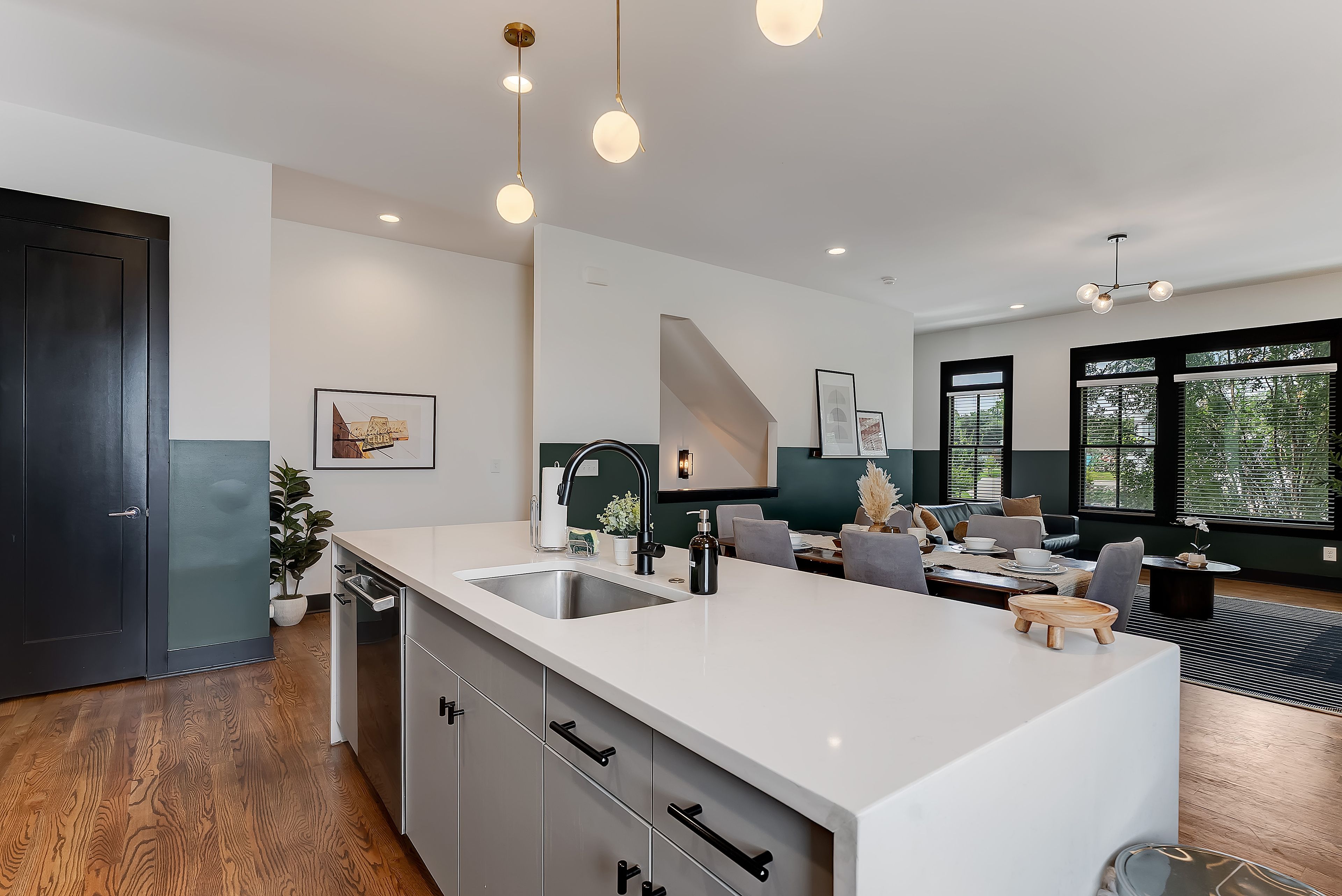 A modern kitchen with a central island, a dining area with a sofa and table, and a view of the outdoors through large windows.