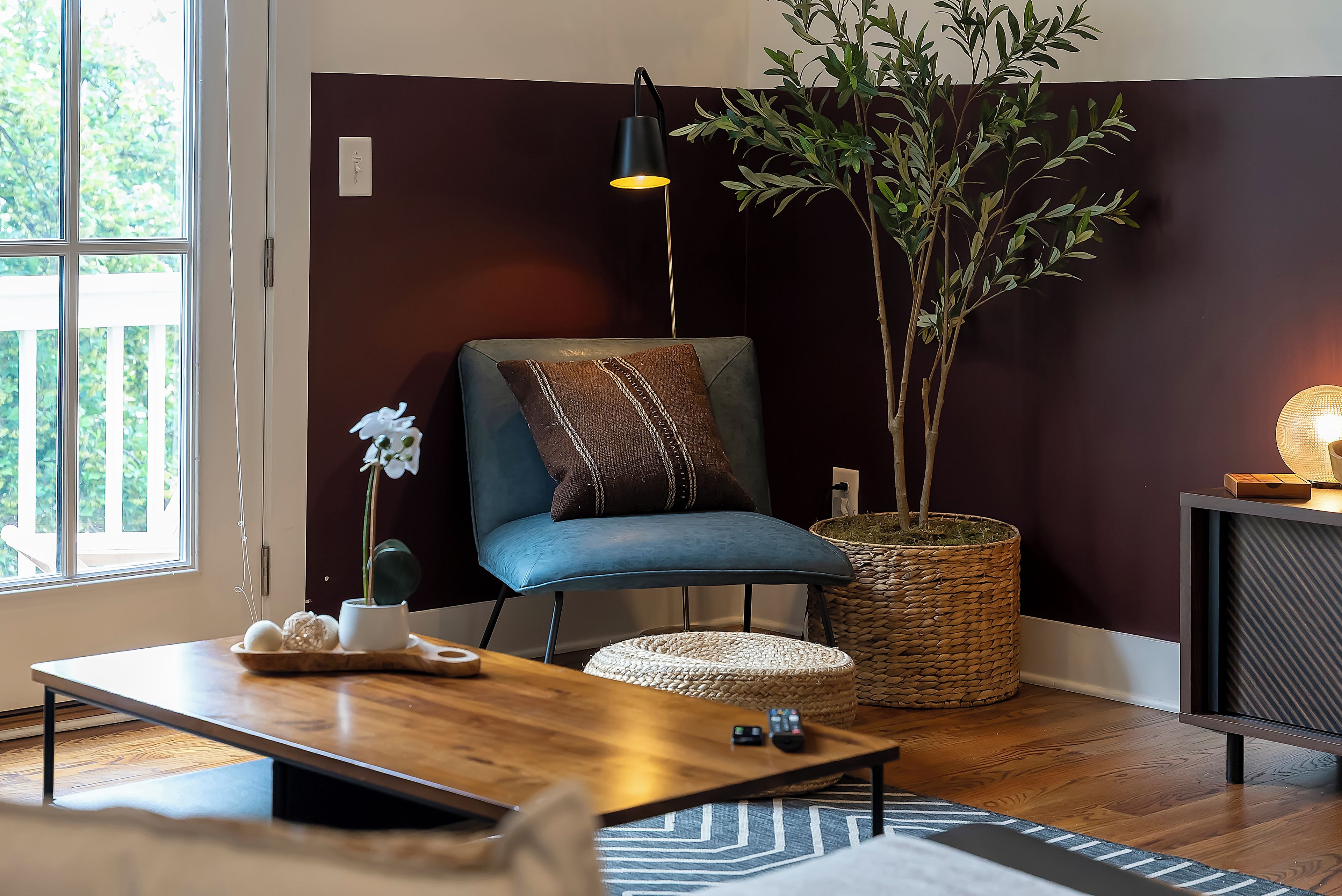 A modern living room with a blue chair, a wooden coffee table, a potted plant, a lamp, and a fireplace.