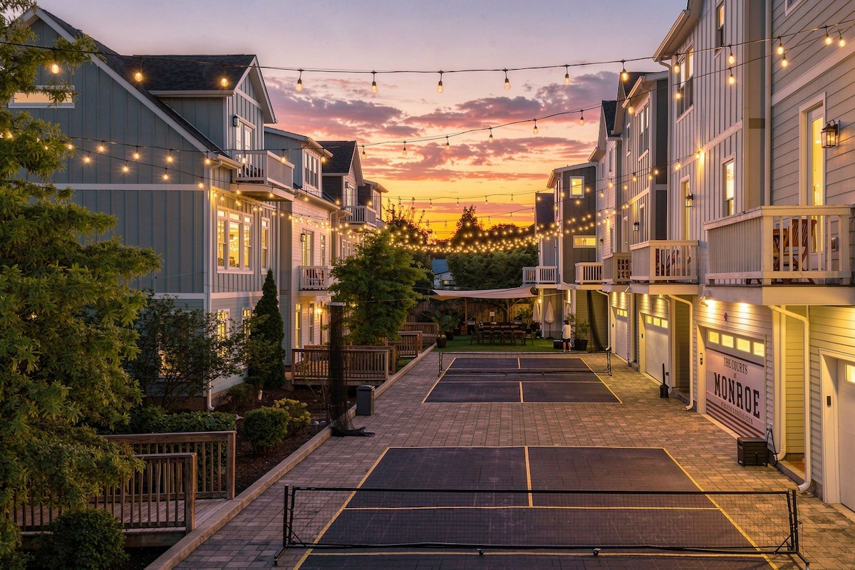 A residential street with houses, string lights, and a tennis court.