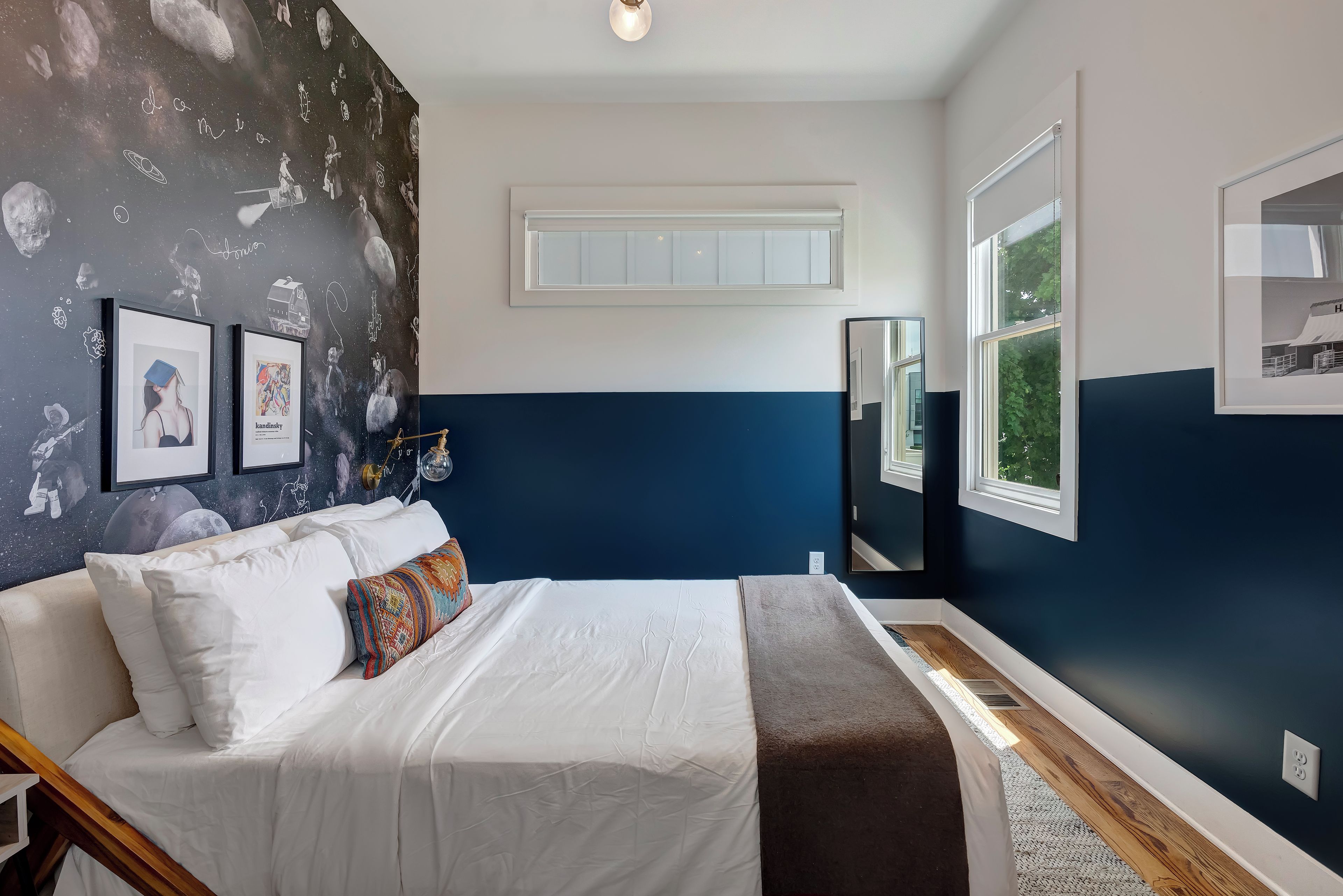 Un dormitorio con cama, un ventanal grande y una pared con un mural de temática espacial.