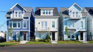 A row of three-story townhouses with front porches, a clear sky, and a street in front. - Monroe Houses (Nashville)