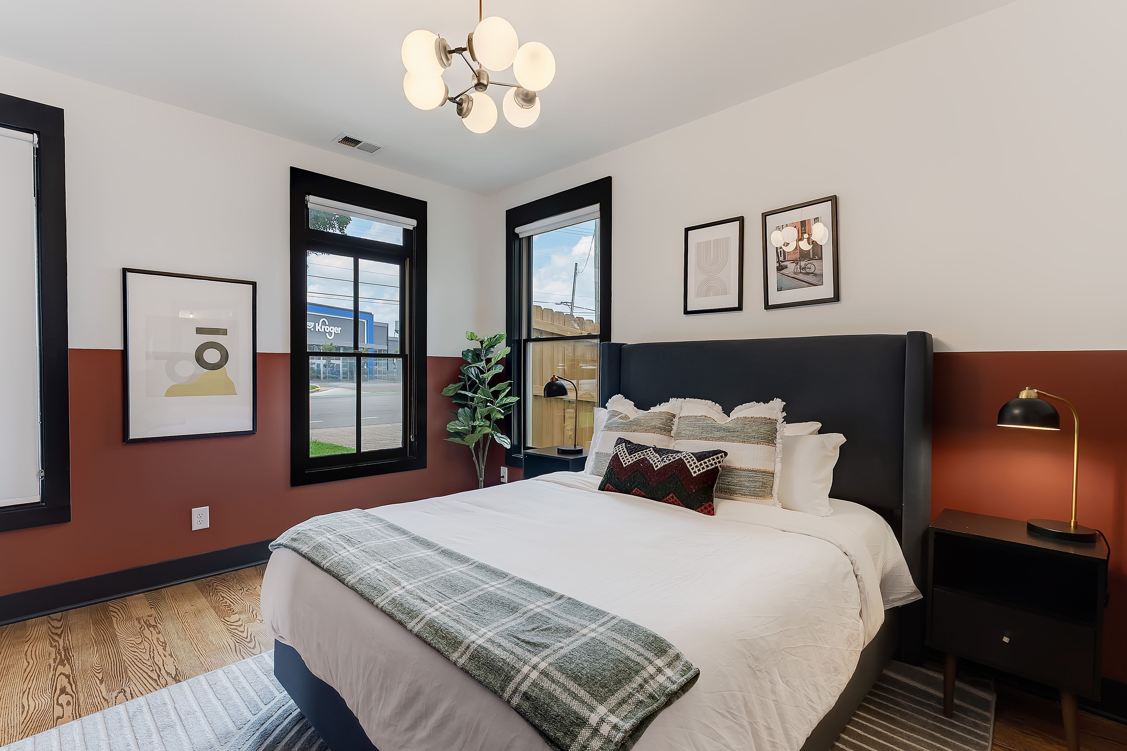 Une chambre à coucher moderne avec un grand lit, une table de chevet, une lampe sur pied et une fenêtre donnant sur la rue.