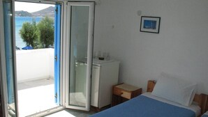 Una habitación con dos camas, un escritorio pequeño, un refrigerador y un ventanal corredero que da a un balcón con vista al mar.