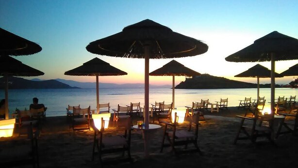 Un área de estar frente a la playa con sombrillas y mesas, con vista al mar.